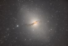 A large bright oddly shaped galaxy with a dark dust band across it